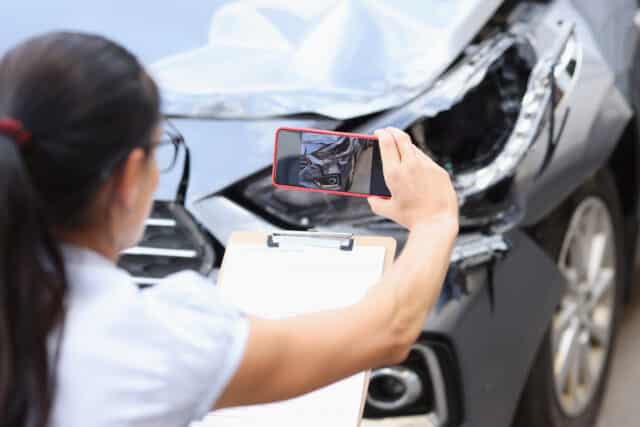 insurance agent takes pictures of damage to car after accident on smartphone